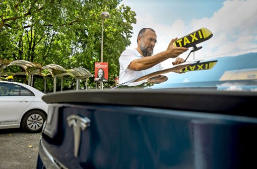Ahmet Gül befestigt sein Taxischild auf seinem Tesla: Nun ist er bereit, seine Kunden elektrisch von A nach B zu fahren. Foto: Lichtgut/Julian Rettig