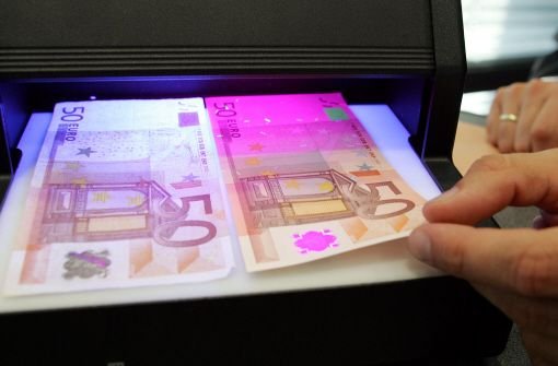 Unter einem UV-Lichtgerät lassen sich Banknoten auf Echtheit prüfen. Links liegt der falsche, rechts der echte 50-Euro-Schein. Foto: AP
