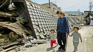 Eine Mutter geht mit ihren zwei Kindern durch eine vom Erdbeben zerstörte Straße in der Präfektur Kumamoto. Foto: dpa