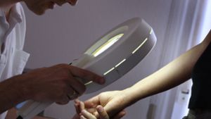 Ein Hautarzt untersucht in seiner Praxis mit einem Vergrößerungsglas die Haut einer Patientin bei einer Hautkrebs-Früherkennung. Foto: picture alliance/dpa