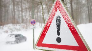 Ein Auto fährt über eine zugeschneite Straße beim nordrhien-westfälischen Bielefeld, daneben ist ein Verkehrsschild mit einem Gefahrenzeichen zu sehen. Foto: Friso Gentsch/dpa