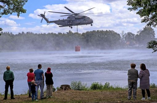 Urlauber beobachten einen Hubschrauber der Bundeswehr beim Aufnehmen von 5000 Liter Löschwasser in einem See. Foto: dpa