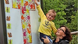 Auf dem Arm von Kindergartenleiterin Ute Schopf zeigt der kleine Simon, welcher Handabdruck von ihm die Schautafel des katholischen Kindergartens ziert. Foto: Sabine Schwieder