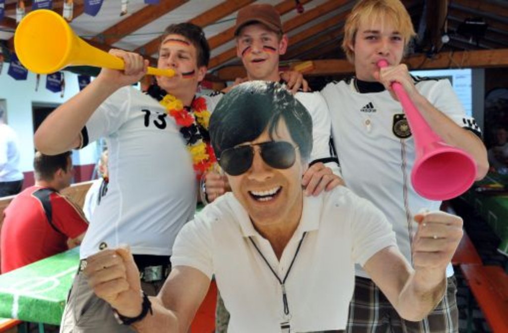 Schönauer Fans des Fußball-Bundestrainers halten im Vereinsheim des lokalen Fußballclubs in Schönau ein lebensgroßes Bild des jubelnden Jogi Löws in den Händen.