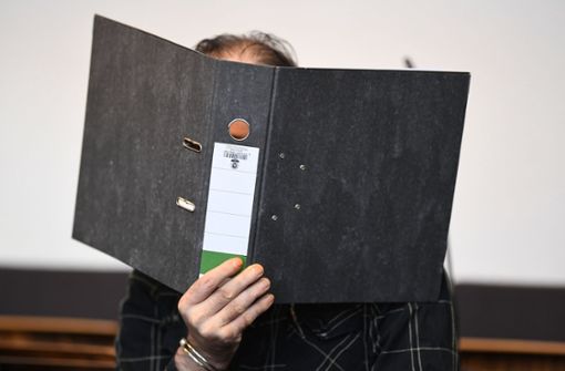 Der wegen Kindesmissbrauchs angeklagte Jürgen W. aus der Schweiz sitzt mit einem Ordner vor dem Gesicht in einem Saal des Landgerichts. Foto: dpa