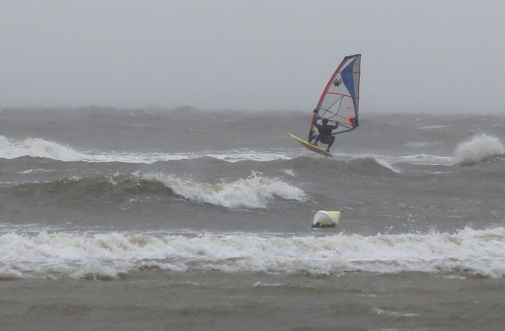 Ein Surfer trotzt dem Wetter und ist bei Sturm auf den Wellen der Nordsee am Strand von St. Peter-Ording unterwegs.