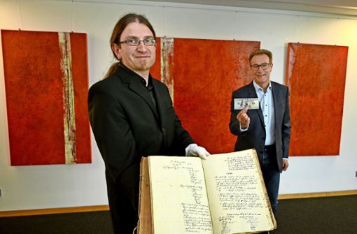 Kreisarchivar Wolfram Berner (links) präsentiert das Original-Gemeinderatsprotokoll von 1844, Schultes Steffen Döttinger die 100 Dollar aus dem Jahr 2021. Foto: Werner Kuhnle
