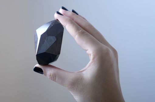 Eine Mitarbeiterin von Sotheby’s Dubai hält den 555,55 Karat schweren Schwarzen Diamanten „The Enigma“ in der Hand, der in der Galerie von Sotheby’s Dubai versteigert werden soll. Foto: dpa/Kamran Jebreili