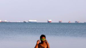 Eine Frau  im Badeanzug am Suez-Kanal – im Hintergrund ist der Stau sichtbar, den das feststeckende Containerschiff ausgelöst hat. Foto: dpa/Ahmed Gomaa