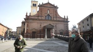 Zwei Männer Menschen mit Mundschutz stehen vor der Kirche San Biagio. In Italien soll die weitere Ausbreitung des Coronavirus mit drastischen Mitteln bekämpft werden. Foto: dpa/Luca Bruno