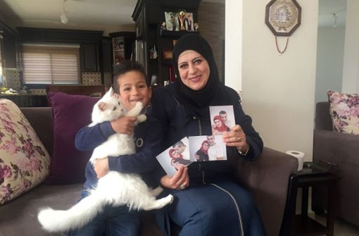 Sohn Madschd (5) und Lydia Rimawi (42) sitzen in ihrem Wohnzimmer auf dem Sofa. In ihren Händen hält Lydia Bilder von sich und ihrem Ehemann Foto: dpa