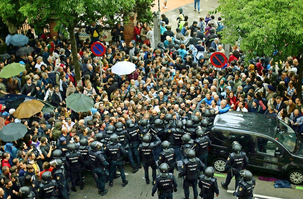 In Barcelona hindern Einheiten der spanischen Nationalpolizei Menschen daran, zum Wahllokal zu gelangen. Vielerorts gelingt die Stimmabgabe dennoch. Separatisten stellen sich in Sant Julia de Ramis mit erhobenen Händen der Polizei entgegen. Foto: AP