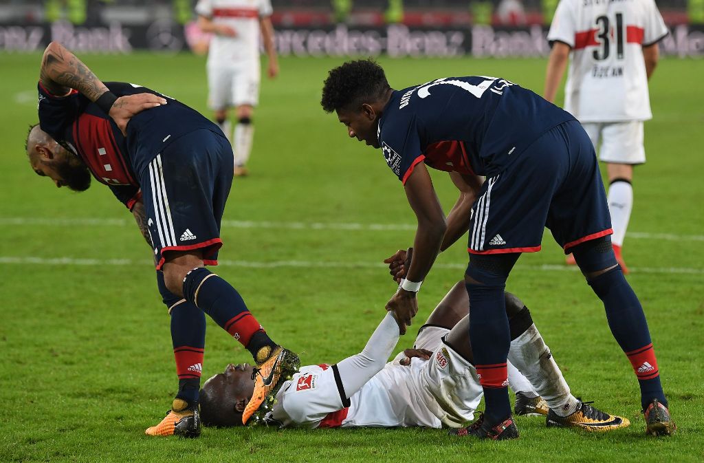 Chadrac Akolo liegt nach seinem verschossenen Elfmeter enttäuscht auf dem Rasen, während die Bayern-Spieler Arturo Vidal (links) und David Alaba den VfB-Stürmer trösten.