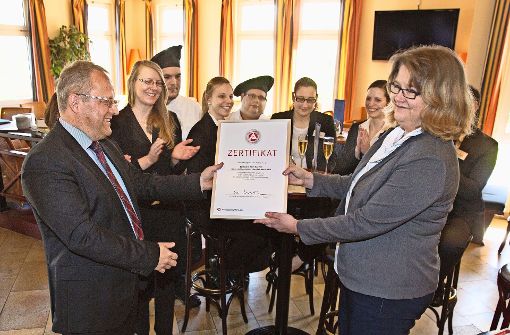 Der Hoteldirektor Andreas Brucker nimmt die Urkunde von Bettina Münz entgegen.  Einige Lehrlinge und ihre Ausbilder sind bei der Auszeichnung dabei und feiern mit. Foto: Rudel