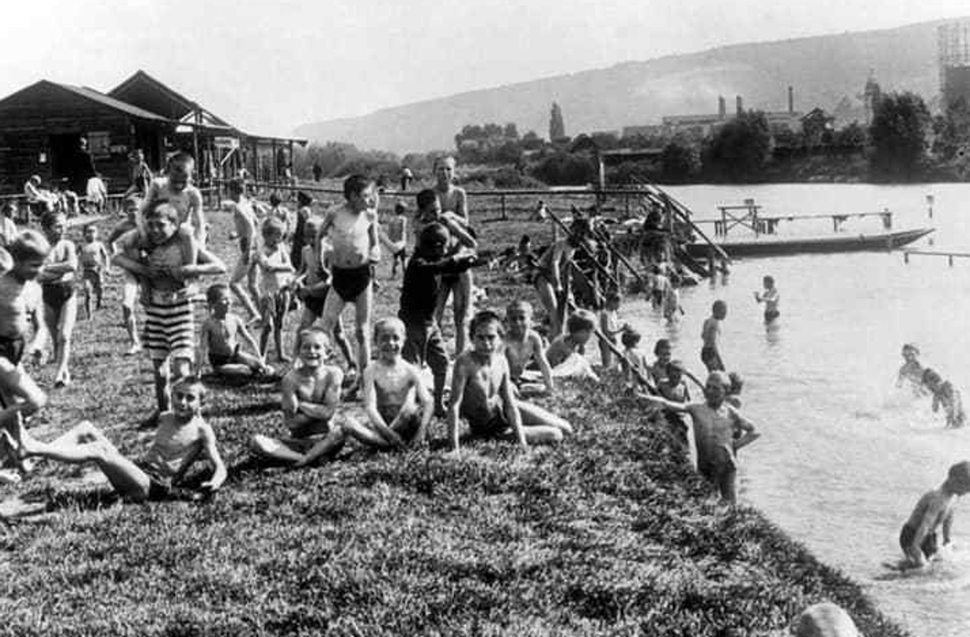 Viele Menschen in Badebekleidung stehen und sitzen auf einer Wiese am Neckar und schauen in die Kamera. Das Bild ist eine schwarz weiß Aufnahme.