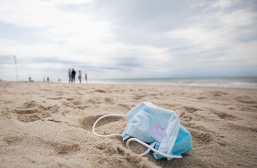 Maske am Strand: ja, der Sommerurlaub 2020 wird besonders. Wo ist man vor Corona einigermaßen sicher? Foto: dpa/Christian Charisius