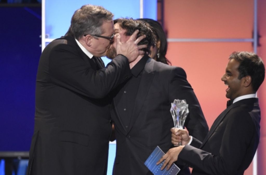 Adam McKay, links, schmatzt Christian Bale bei dessen Triumph in der Kategorie „Beste Komödie“  für “The Big Short”.  Aziz Ansari, der die Auszeichnung überreicht, freut’s. Foto: dpa