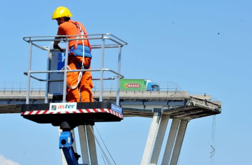 Genua: Ein Arbeiter steht im Korb eines Krans, im Hintergrund ist die eingestürzte Morandi-Autobahnbrücke zu sehen. Foto: dpa