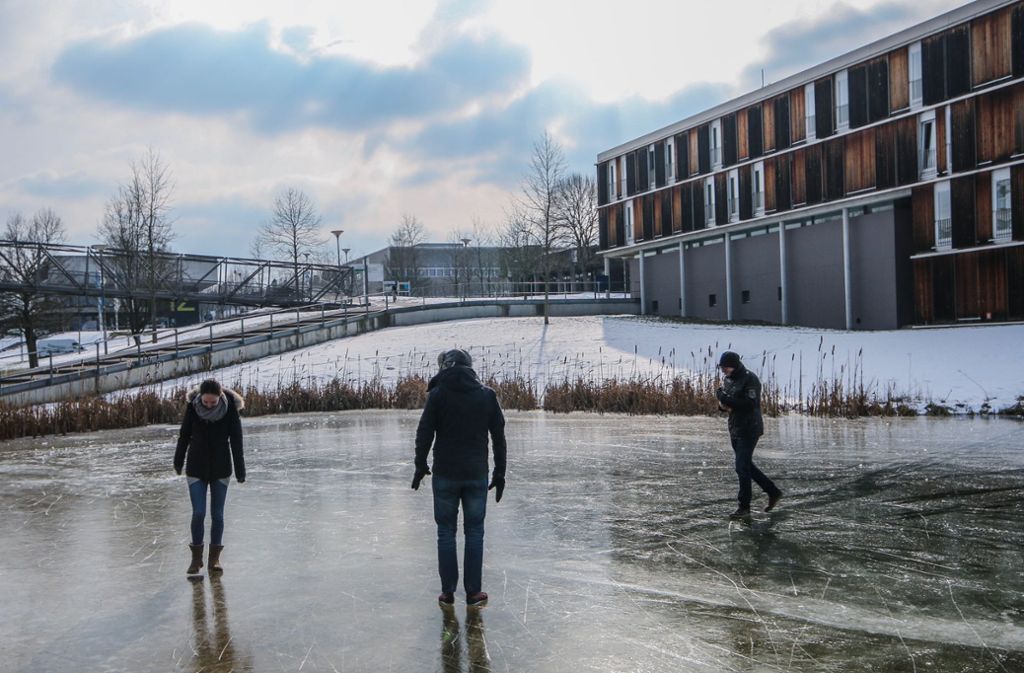 Studenten auf dem Vaihinger Uni-Campus spazieren über einen zugefrorenen Teich.