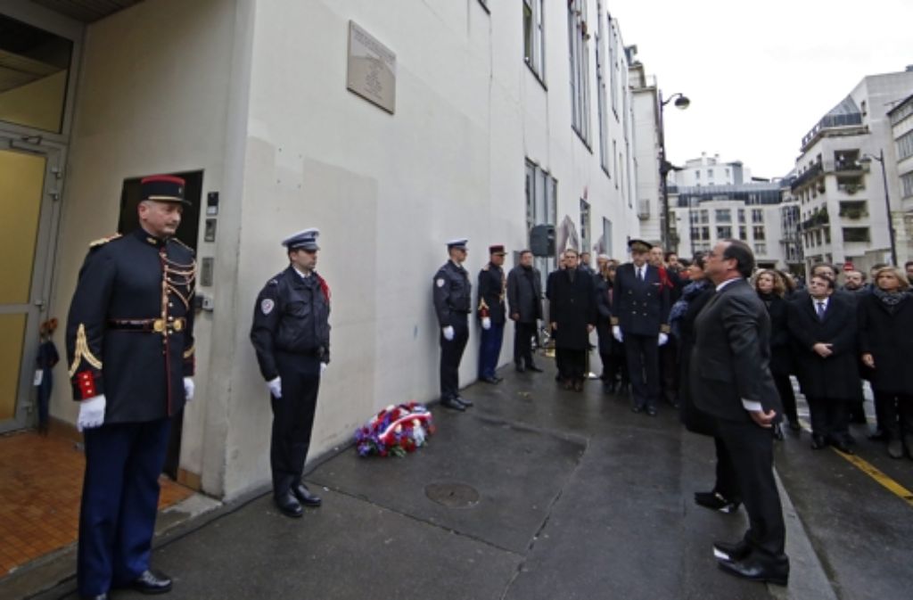 Hollande steht vor einer Gedenktafel, die außen an der Charlie-Hebdo-Redaktion angebracht wurde.