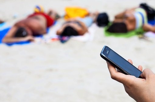 Eine deutsche Urlauberin schreibt  an einem polnischen Strand mit einem Mobiltelefon eine SMS. Roaminggebühren fallen 2017 im EU-Ausland weg Foto: dpa