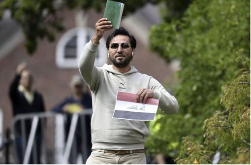 Ein  Demonstrant hält eine Taschenbuchausgabe des  Korans hoch, die er mutmaßlich gemeinsam mit einer irakischen Fahne vor der irakischen Botschaft in Stockholm verbrennen will  (Foto vom 20. Juli 2023). Foto: TT NEWS AGENCY/AP/dpa/Oscar Olsson