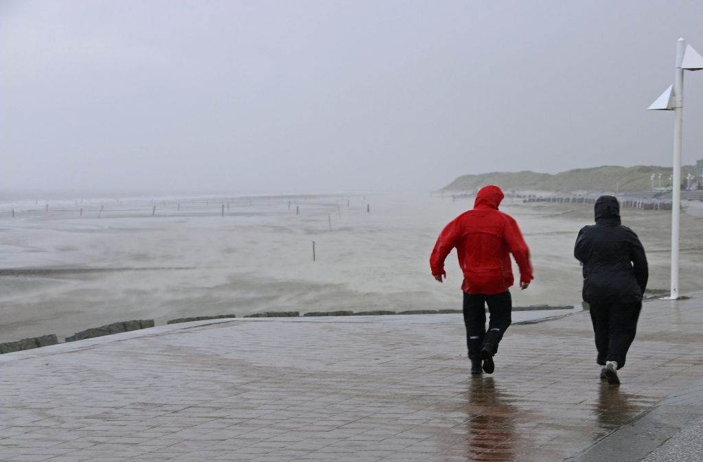 Zwei Passanten in Regenkleidung gehen auf Norderney bei stürmischem Wetter die Strandpromenade entlang.