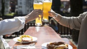 Tübingen: Zwei Menschen sitzen bei gutem Wetter in einem Biergarten und stoßen mit einem Bier an. In Tübingen können Menschen in der Stadt kostenlose Corona-Tests machen. Foto: dpa/Tom Weller