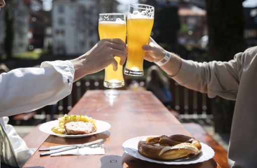 Tübingen: Zwei Menschen sitzen bei gutem Wetter in einem Biergarten und stoßen mit einem Bier an. In Tübingen können Menschen in der Stadt kostenlose Corona-Tests machen. Foto: dpa/Tom Weller