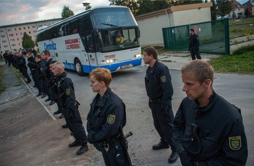 Polizisten stehen in Bischofswerda (Sachsen) vor einem Bus, der Flüchtlinge in eine Notunterkunft bringt. Mehr als 50 Menschen versammelten sich am Freitagabend vor dem früheren Bekleidungsbetrieb und skandierten fremdenfeindliche Parolen Foto: dpa