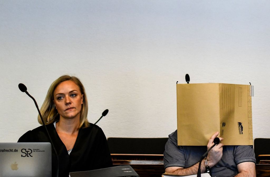 Der wegen Kindesmissbrauchs angeklagte Mann sitzt in Handschellen im Gerichtssaal neben seiner Verteidigerin Mona Hammerschmidt (links) und hält einen Aktendeckel vor sein Gesicht. Foto: dpa