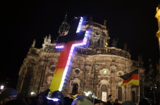 Anhänger des Pegida-Bündnisses (Patriotische Europäer gegen die Islamisierung des Abendlandes) demonstrieren in Dresden  gegen die angebliche Überfremdung durch Flüchtlinge und halten ein Kreuz in den Landesfarben schwarz-rot-gold in die Höhe. Foto: dpa