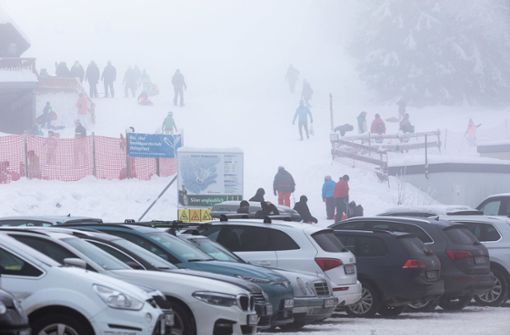 Menschen stehen im dichten Nebel nahe dem Skilift am Haldenköpfle, während im Vordergrund der volle Parkplatz der geschlossenen Liftanlage zu sehen ist. Foto: dpa/Philipp von Ditfurth