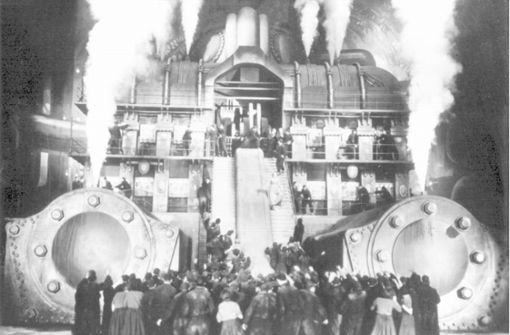 Eine aufgebrachte Menschenmenge steht vor einem dampfenden Maschinengebäude – Szene aus „Metropolis“ (Archivfoto von 1926). Der legendäre Stummfilm von Fritz Lang aus der goldenen UFA-Ära wurde  2001 als erster Film in das Unesco-Weltdokumentenerbe aufgenommen. Foto: dpa