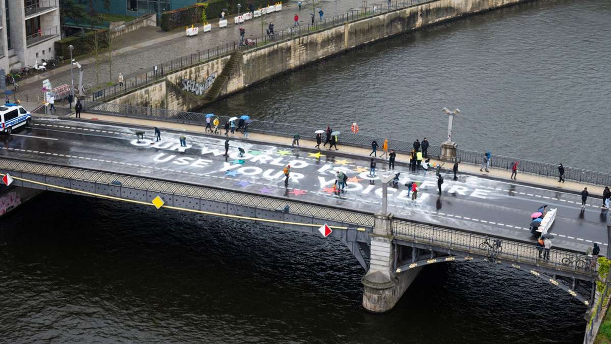 Klimaaktivisten der Bewegung Fridays for Future malen auf der Marschallbrücke in Berlin den Schriftzug Our world is on fire - use your voice!.