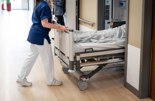 Eine Pflegekraft schiebt einen Patienten im Krankenbett in ein Krankenzimmer (Symbolbild). Foto: IMAGO/Political-Moments/IMAGO