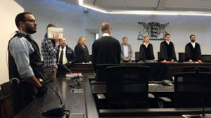 Ein wegen Mordes angeklagter Mann (2. von links) verdeckt in einem Verhandlungssaal des Landgerichts sein Gesicht mit einem Aktenordner. Foto: dpa