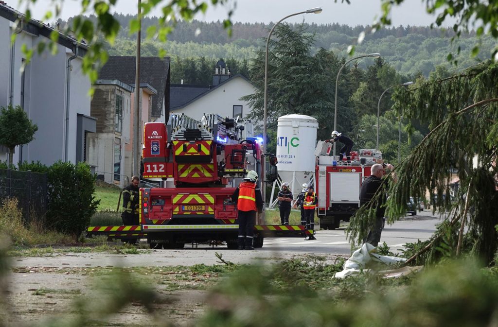 Nach dem  schweren Unwetter mit einem Tornado räumen Feuerwehrleute  in der  Stadt Pettingen im Südwesten Luxemburgs  eine Straße frei. Mehrere Menschen wurden durch die Folgen des Unwetters nach Angaben der luxemburgischen Regierung verletzt –  einige davon schwer..