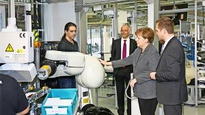 Eingerahmt vom Werksleiter Stefan Schwerdtle (rechts) und dem Vorstandsvorsitzenden von Festo, Claus Jessen, berührt Angela Merkel bei ihrem Rundgang durch die Fabrik Uschi –  den ersten Roboter, der keinen Käfig braucht. Foto: Horst Rudel