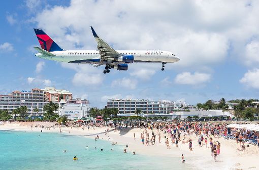 Am Maho Beach auf Sint Maarten fliegt ein Flugzeug dicht über die Badegäste hinweg auf die Landebahn des Fluhafens zu. (Archivfoto) Foto: dpa