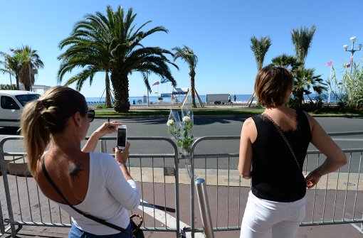 Eine Frau fotografiert die Rosen, die in die Absperrung an der Promenade in Nizza gesteckt wurden. Foto: dpa