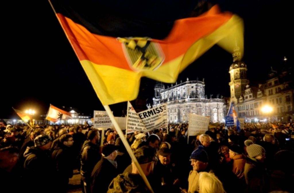 Anhänger des Pegida-Bündnisses (Patriotische Europäer gegen die Islamisierung des Abendlandes) demonstrieren in Dresden gegen die angebliche Überfremdung durch Flüchtlinge und schwenken eine Deutschlandfahne. Foto: dpa