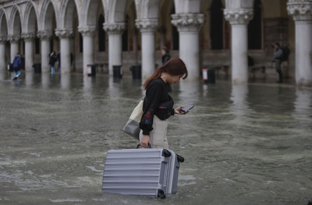Überschwemmungen in Venedig. Eine Frau wartet mit ihrem Koffer durch das Wasser auf dem Markusplatz.