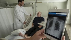 Oberarzt Michael Svoboda bei einem seiner Patienten. Röntgenbilder  kann er nun  direkt am Bett  auf dem Tablet zeigen. Foto: factum/Weise