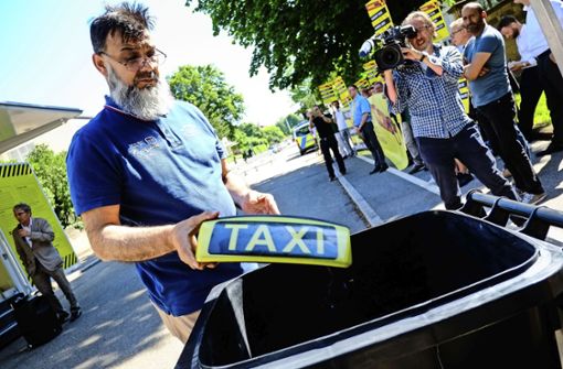 Taxifahrer werfen vor dem Stuttgarter Staatsministerium symbolisch Taxischilder in eine Mülltonne. Sie fürchten das Ende ihrer Branche. Foto: Max Kovalenko