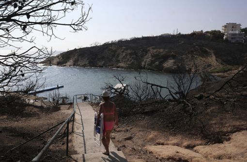 Eine Frau geht beim griechischen Badeort Rafina hinunter zum Strand. Rechts und links vom Weg sieht man, wie das Feuer vor zehn Tagen gewütet hat. Foto: AP