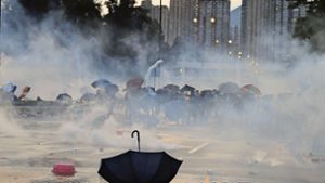 Ein Regenschirm liegt auf einer Straße, während Demonstranten vor Tränengas in Deckung gehen. Foto: picture alliance/dpa/Kin Cheung
