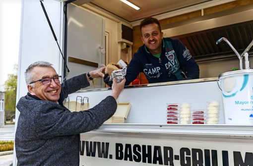 Bürgermeister Ekkehard Fauth lässt sich gegen seinen knurrenden Magen einen Cheeseburger reichen. Der Syrer Kadan Bashar  mit Lebensmittelpunkt in Aidlingen hat sich mit einem Imbisswagen selbstständig gemacht. Foto: Stefanie Schlecht