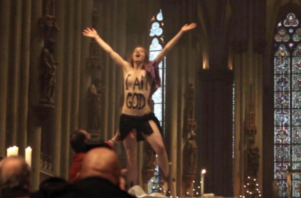 Eine Femen-Aktivistin posiert am 25. Dezember 2013 mit bemaltem Oberkörper I am God während der Weihnachtsmesse im Kölner Dom auf dem Altar.  Foto: dpa