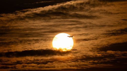 Der Tag geht zu Ende: Ein Flugzeug fliegt vor der untergehenden Sonne über Frankfurt am Main. Foto: Boris Roessler/dpa